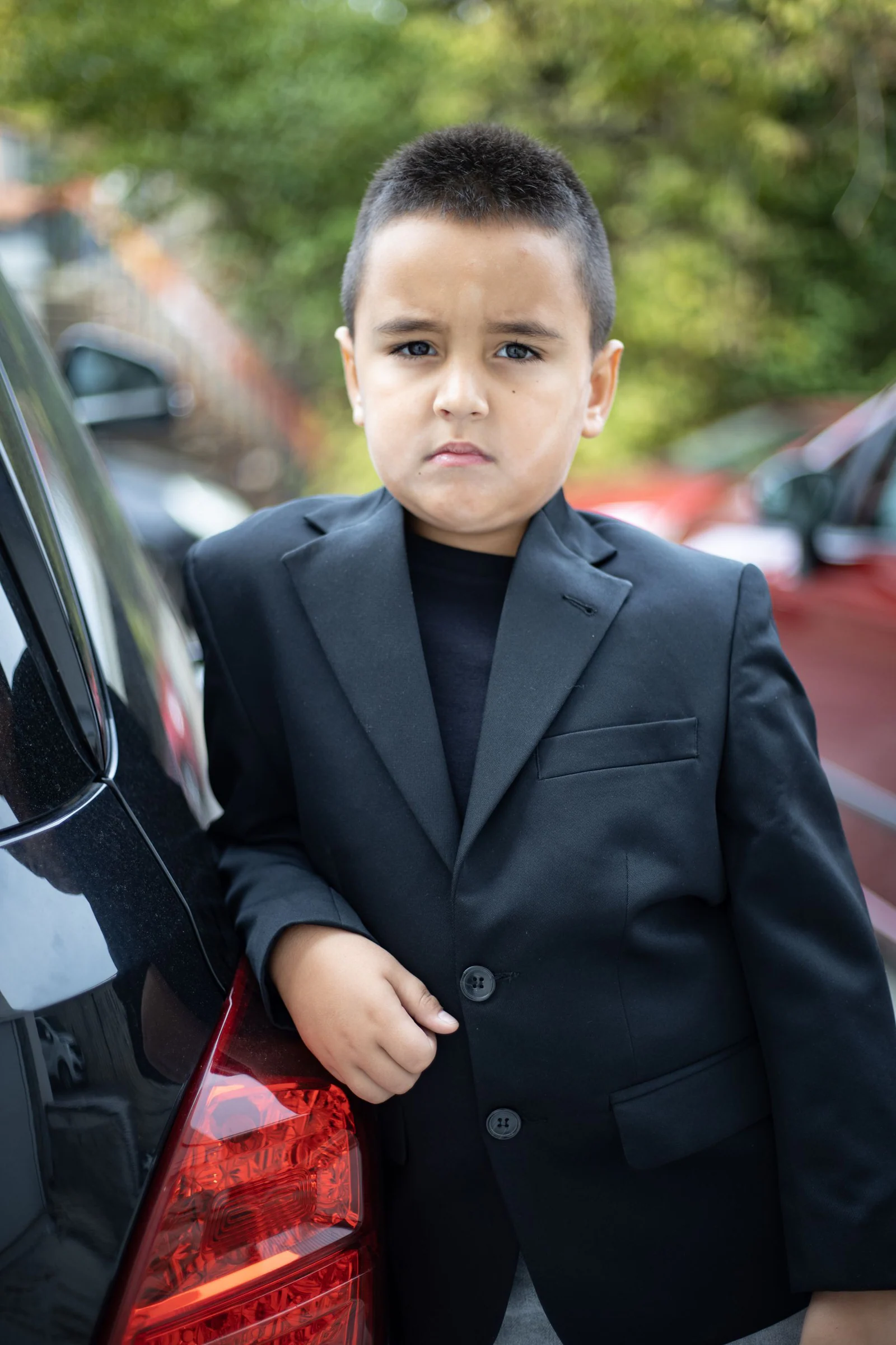 Young boy in suit standing by a car outside