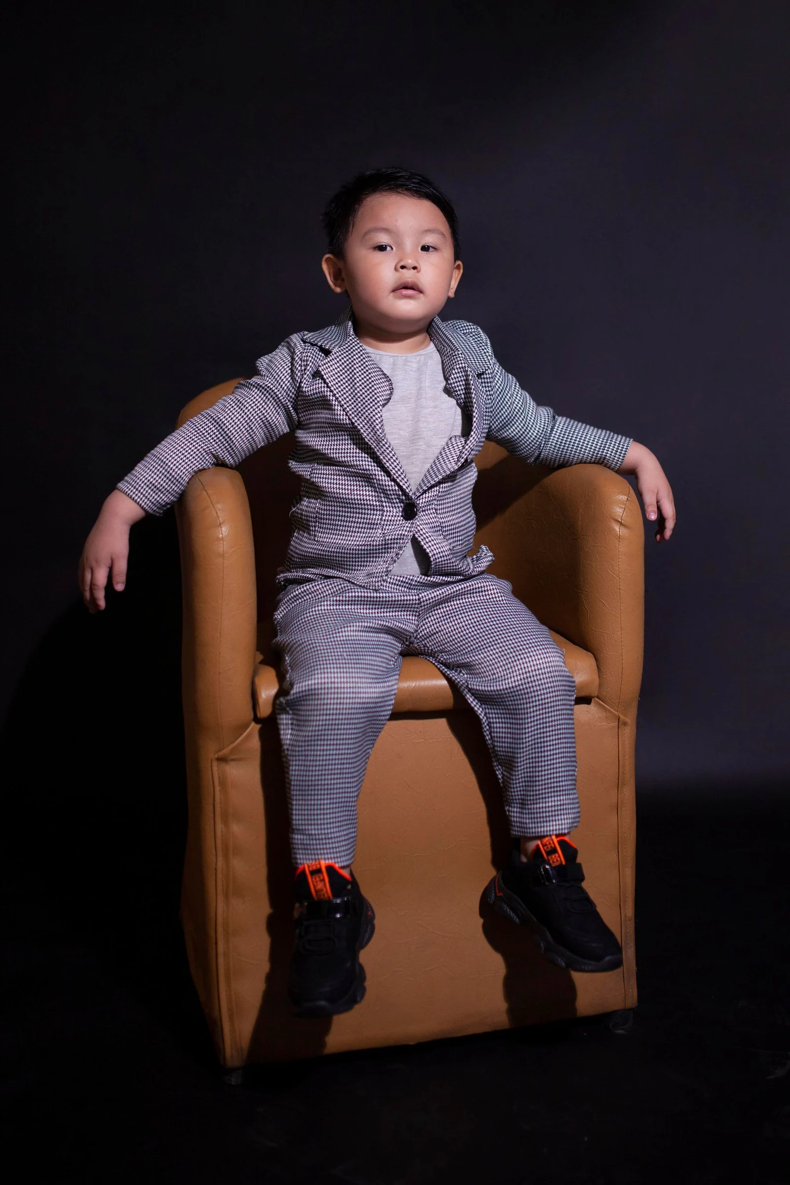 Boy wearing a suit sitting on brown sofa chair
