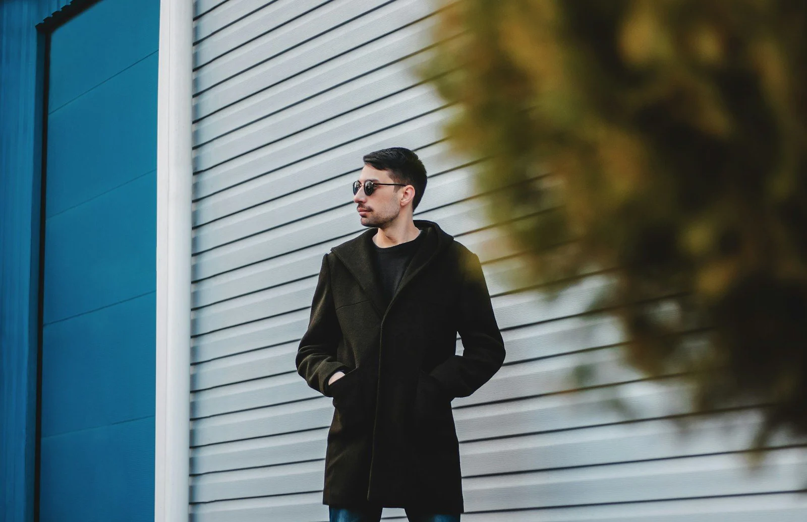 Man in black coat standing beside building during daytime