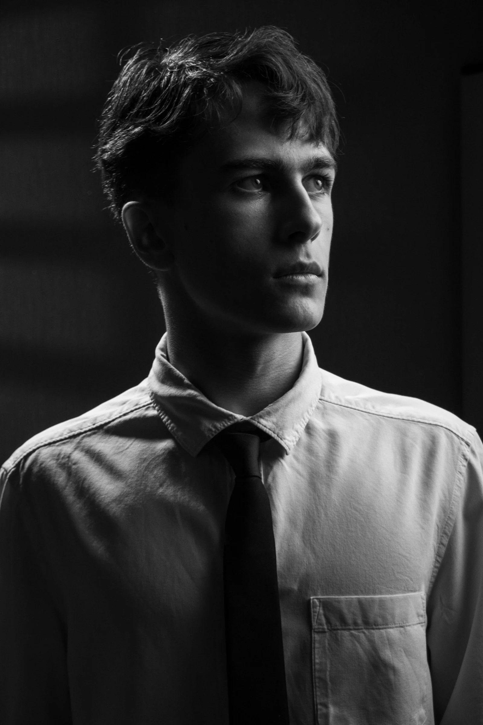 A young man in a shirt and tie looking away