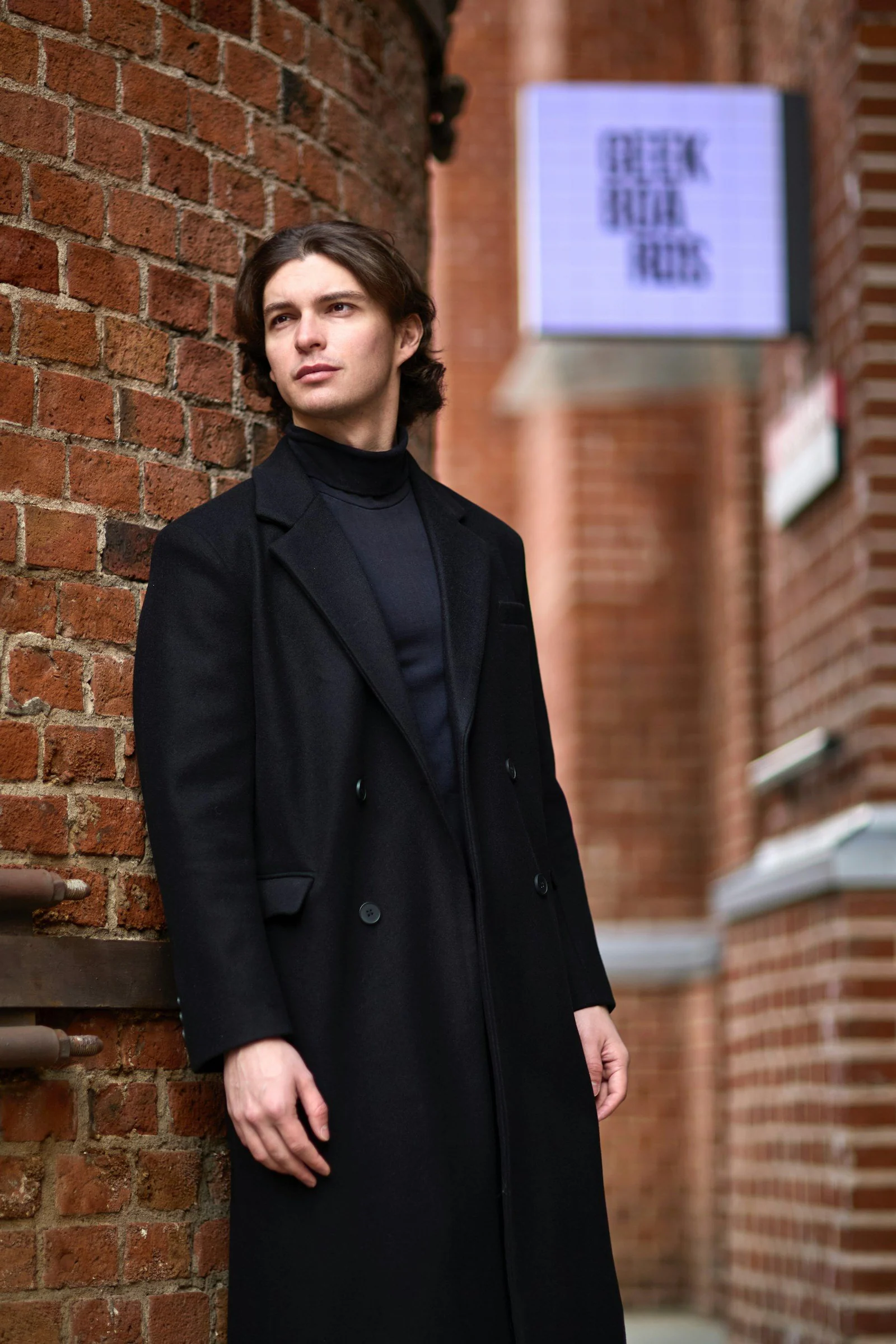 A man leans against a brick wall
