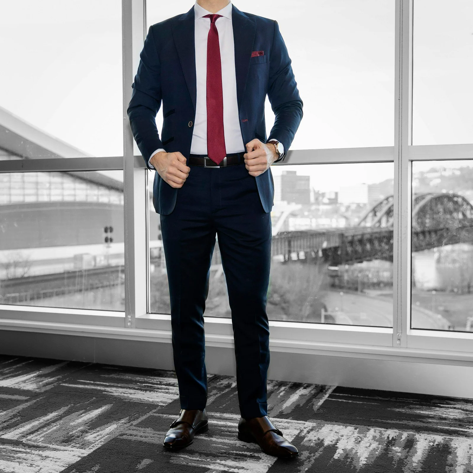 Man in blue dress shirt and blue denim jeans standing near glass window