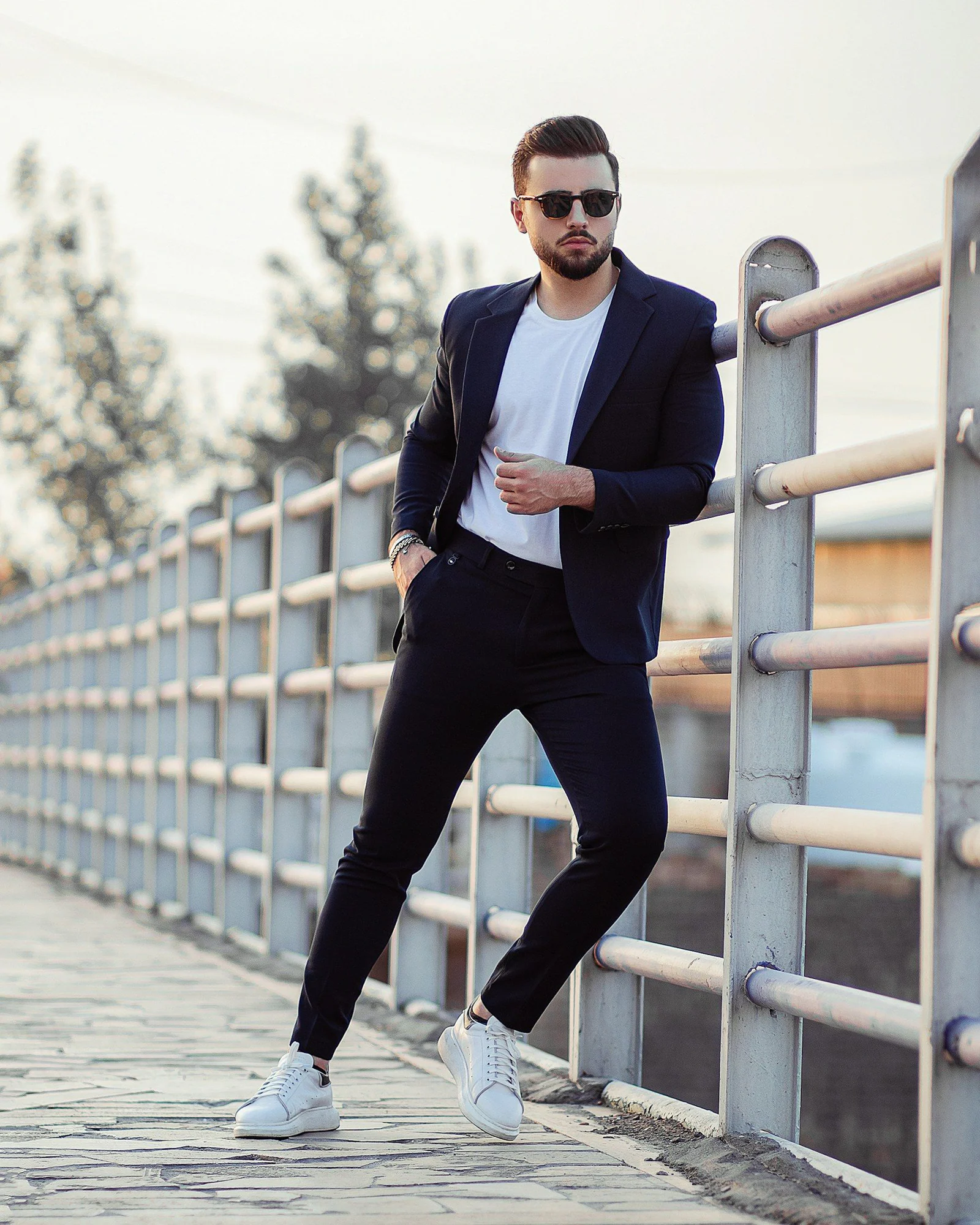 Man in black blazer and blue denim jeans leaning on brown wooden railings during daytime