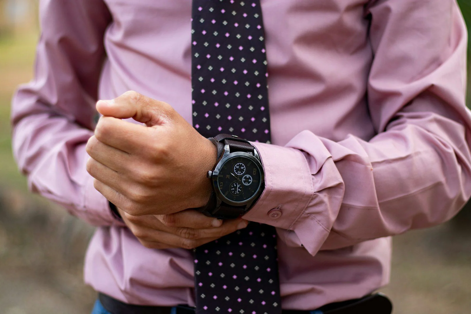 Man wears black chronograph watch and pink dress shirt