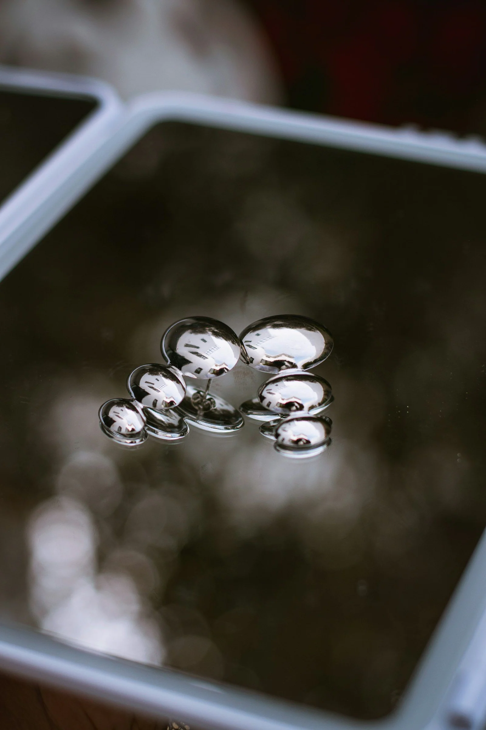 Shiny mercury drops on a dark reflective surface