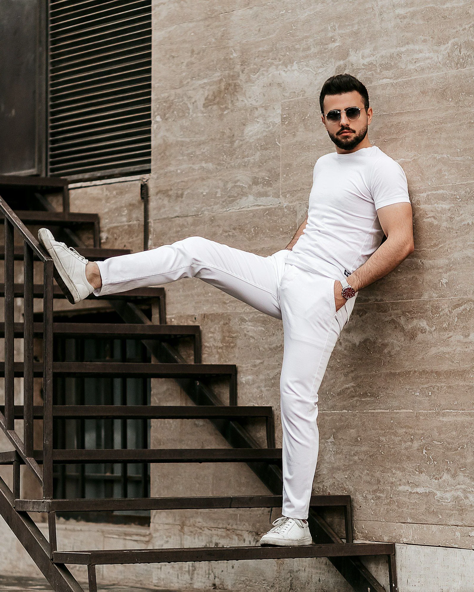Man in white t shirt and white pants standing on black wooden stairs