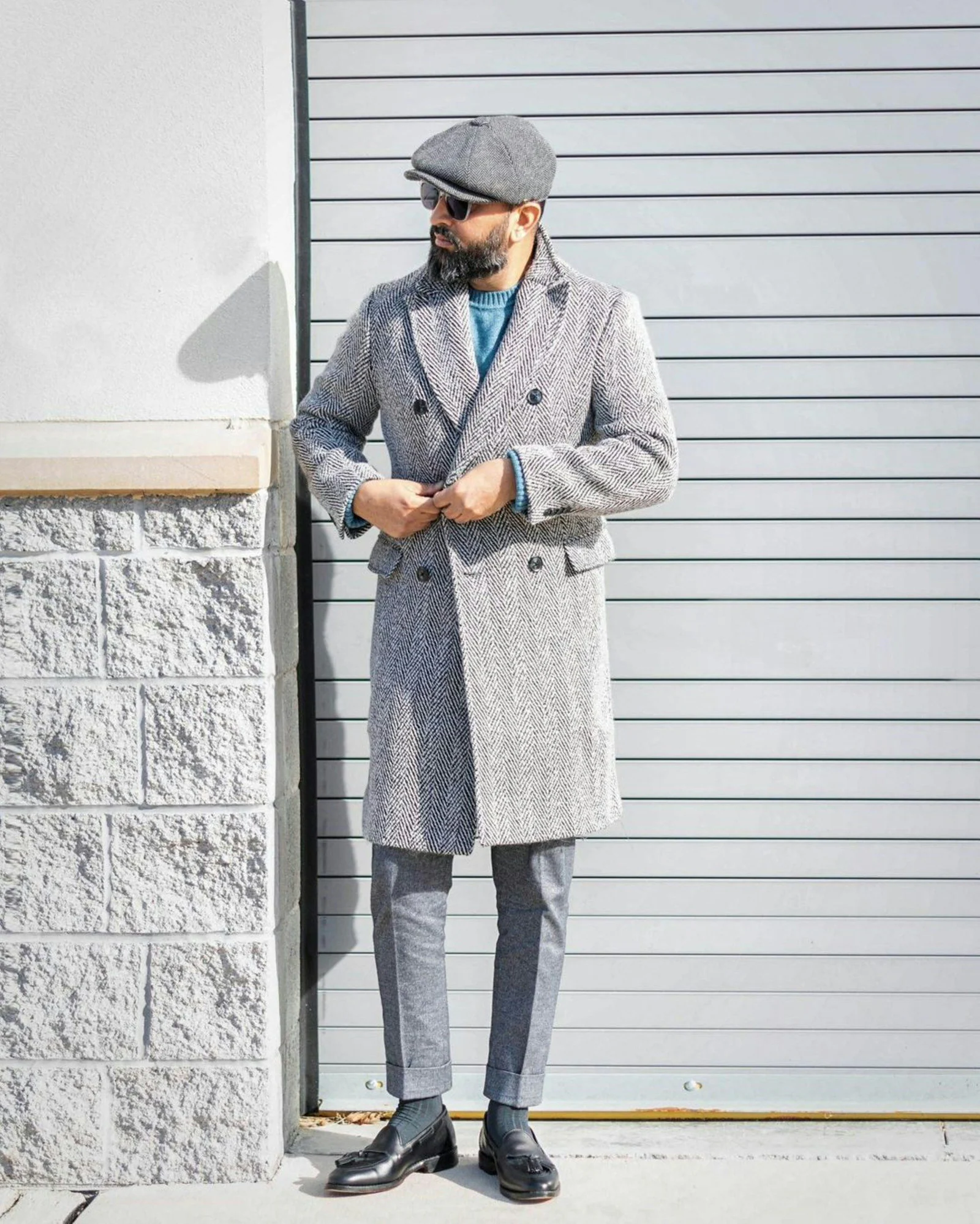 A man in a gray coat and hat standing in front of a garage door
