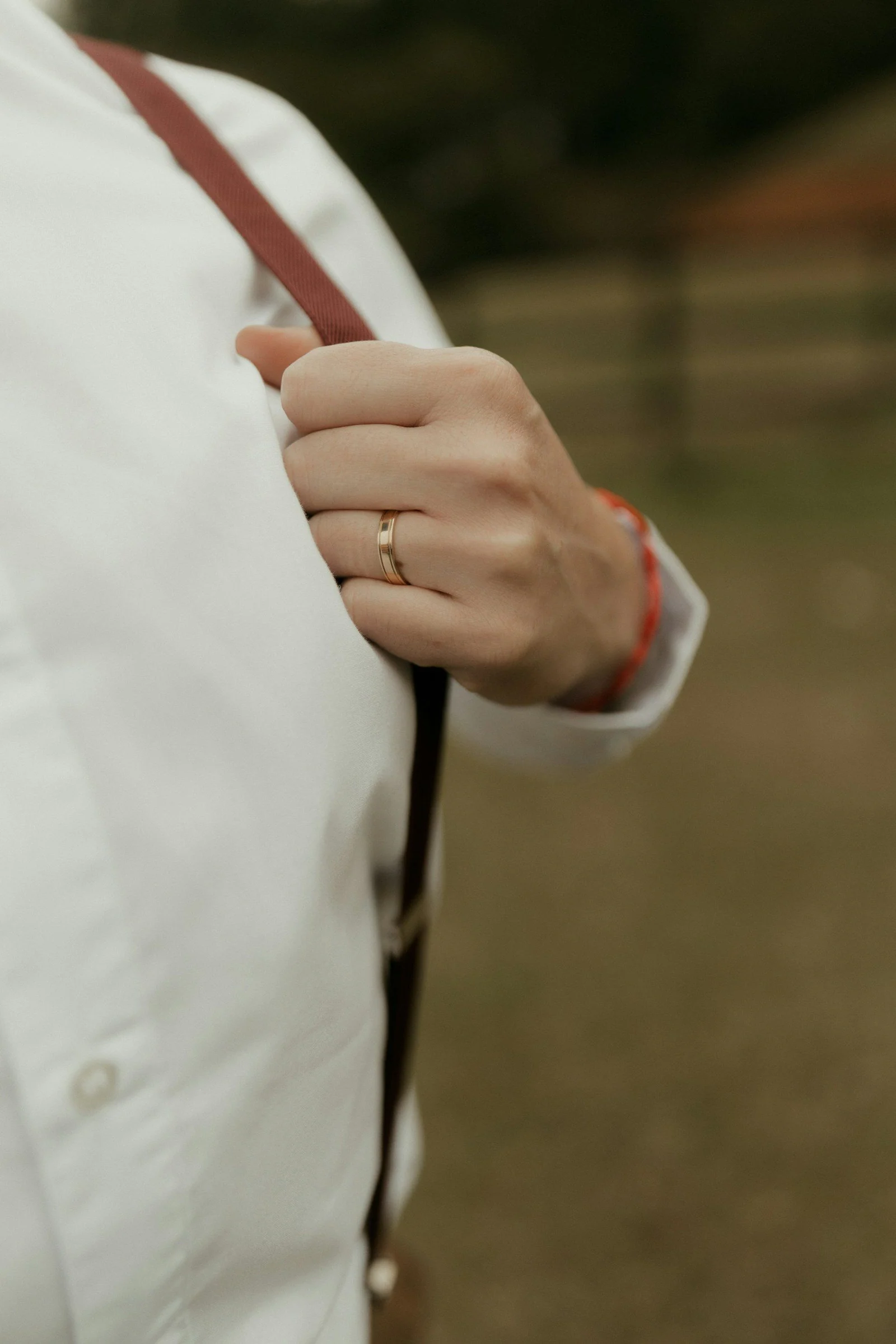 A hand with a ring holding a red suspender strap