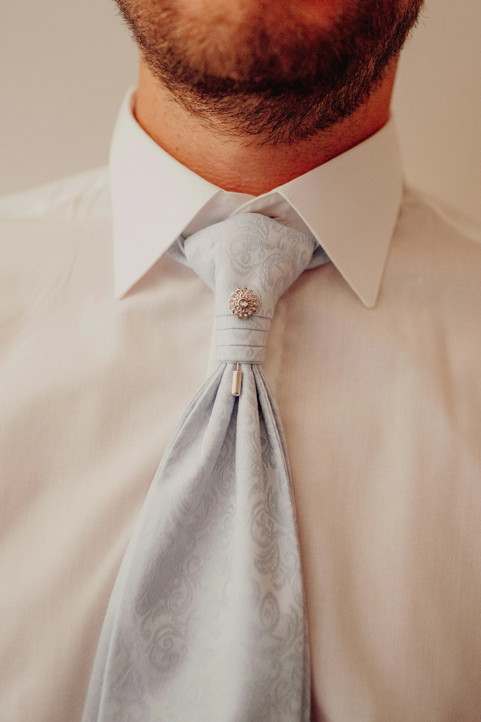 Mans white shirt and blue patterned cravat with a pin