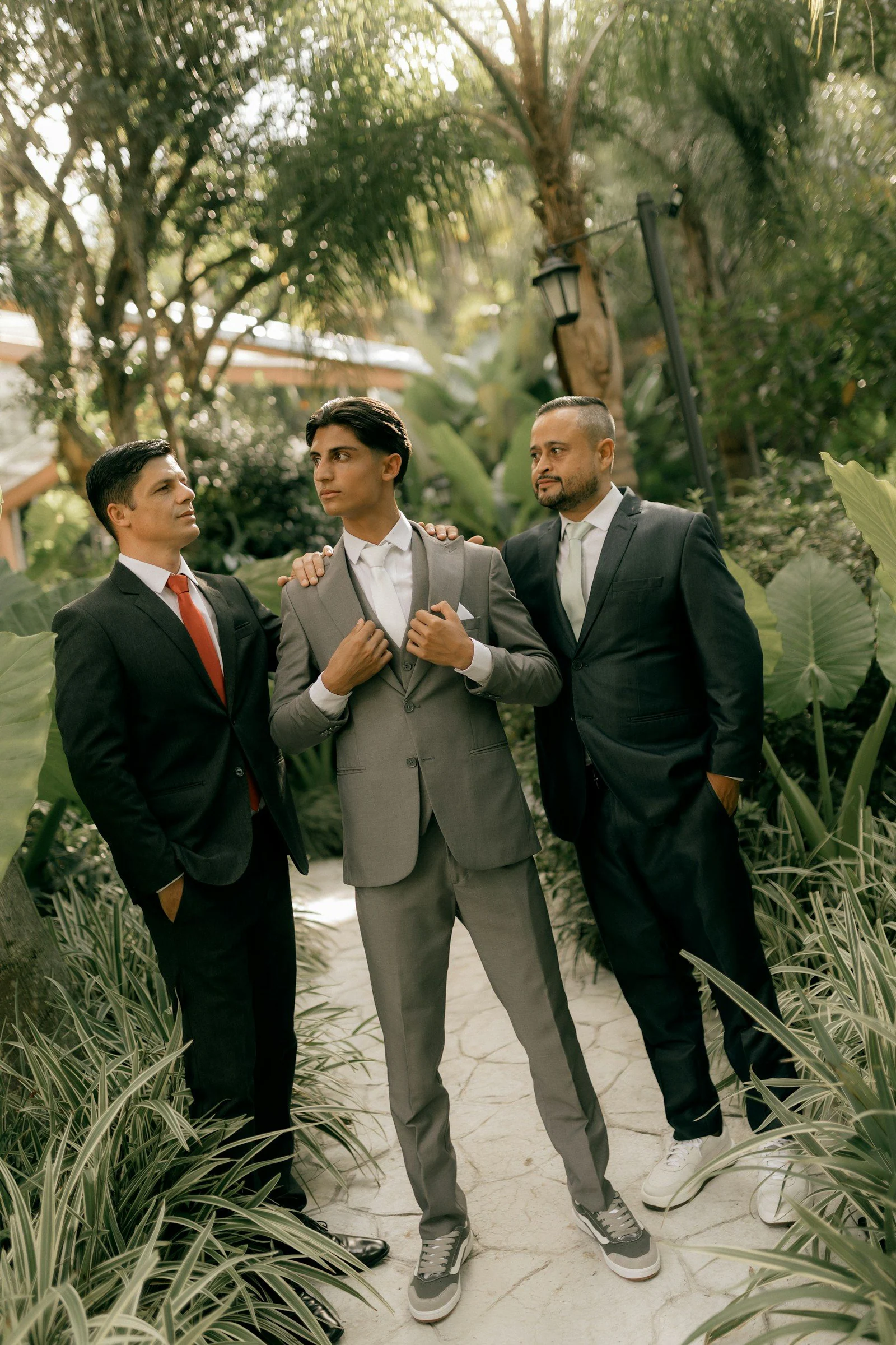 Three men in suits standing outdoors among plants