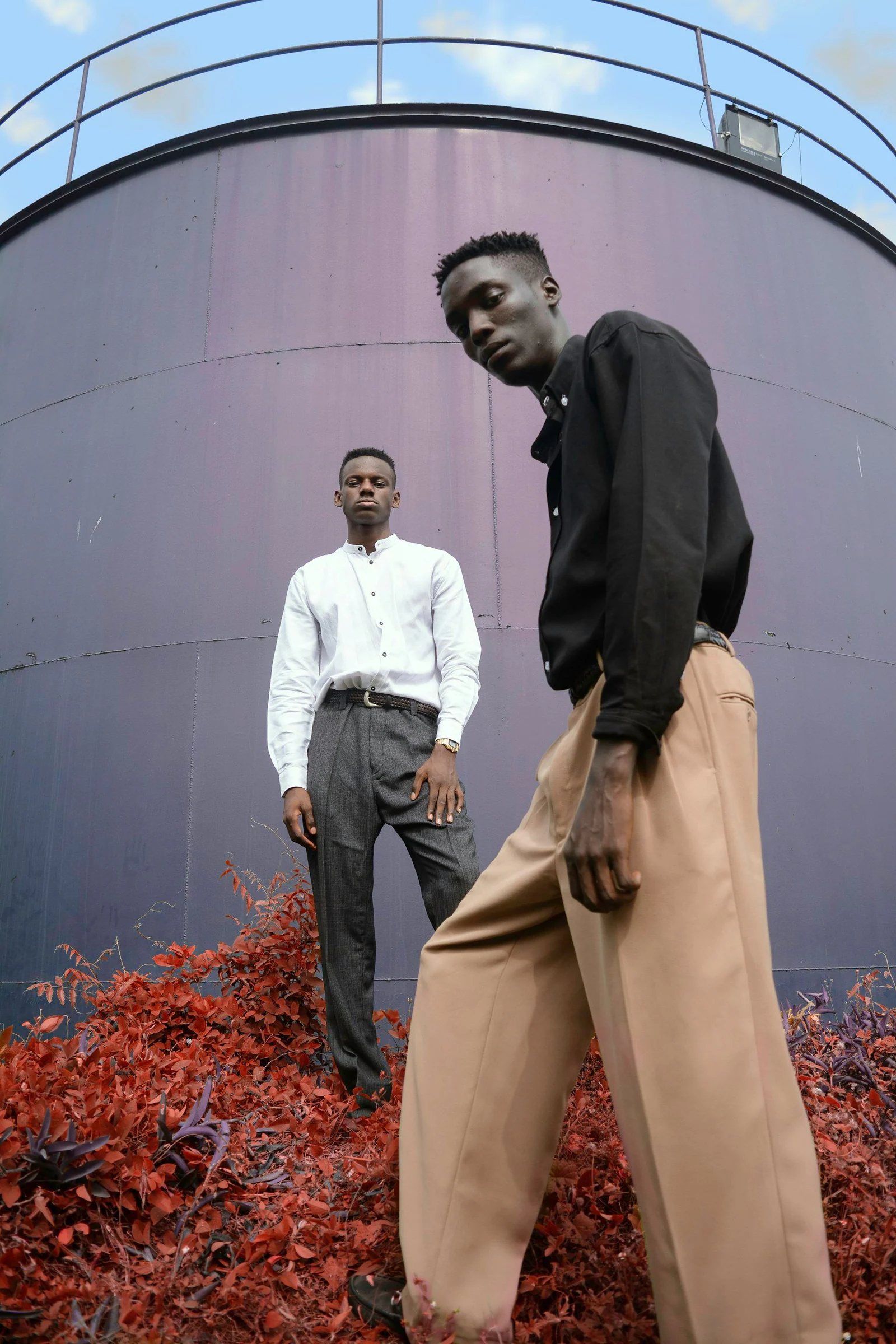 Two men standing on red flower in front of gray metal wall