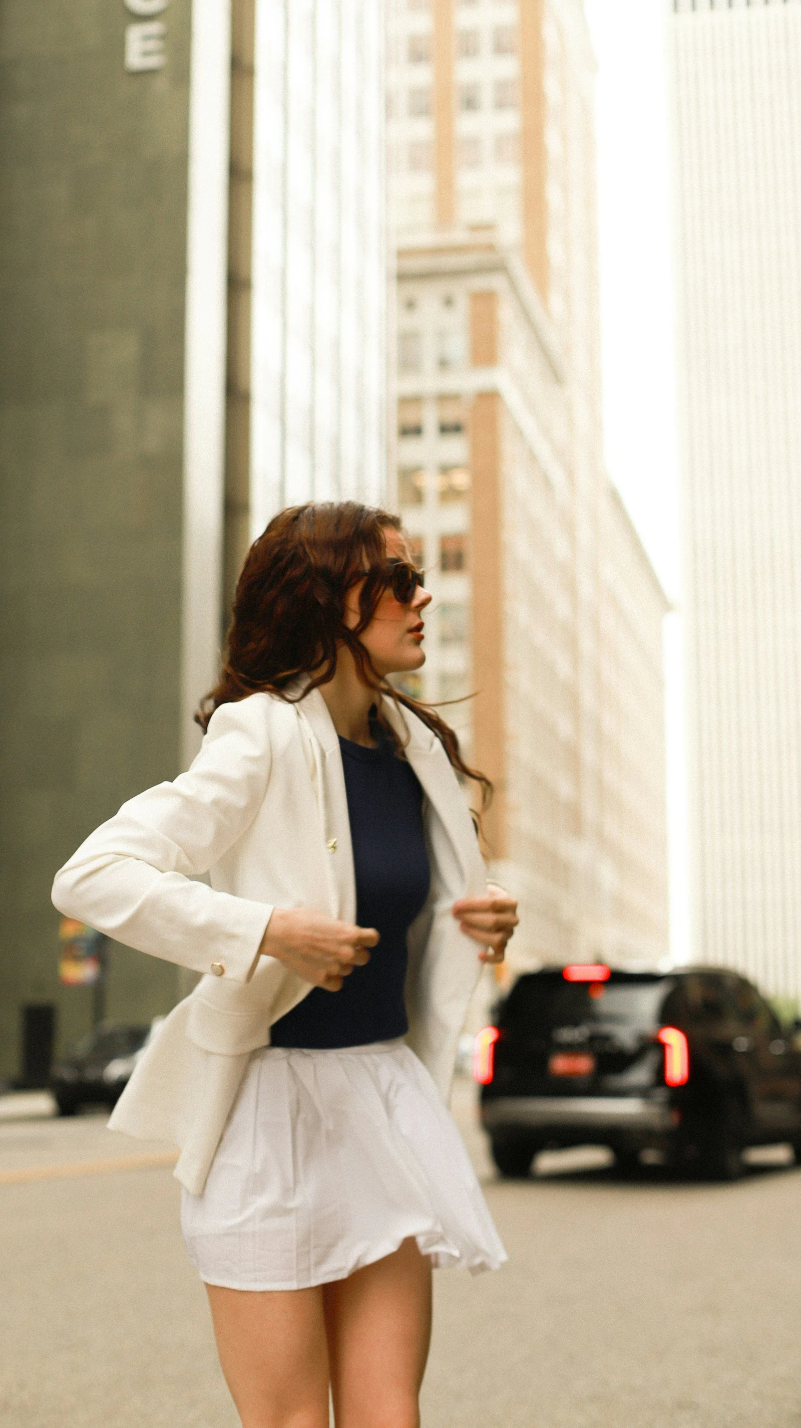 Woman in white blazer and skirt walking on city street
