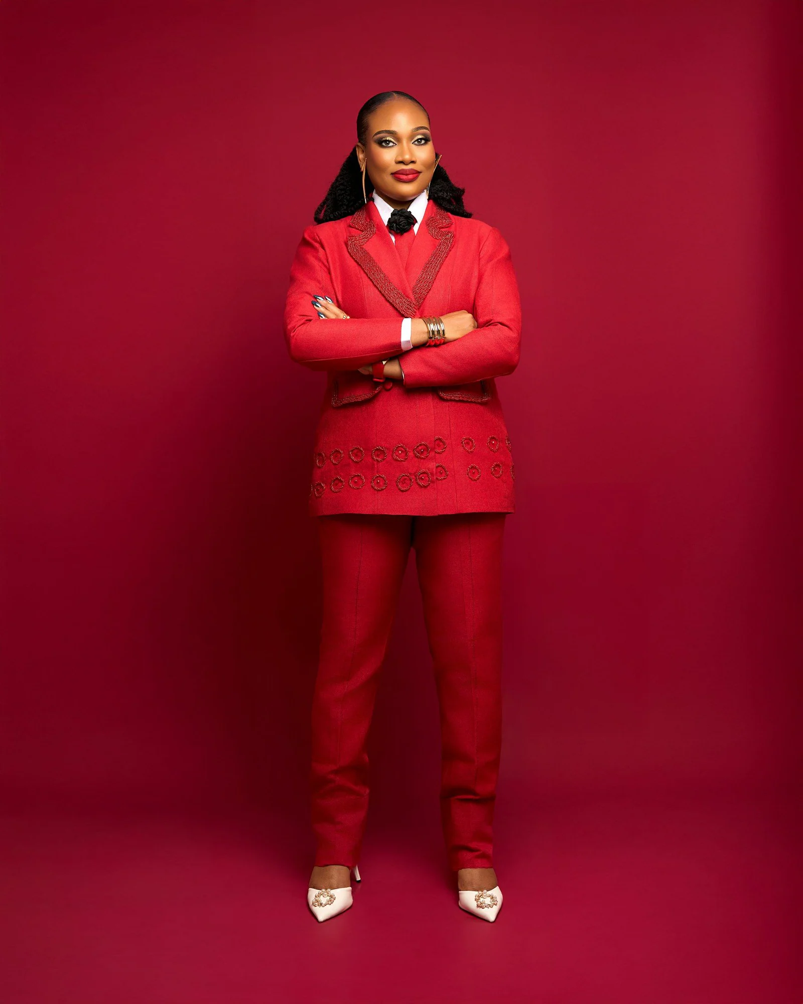 A woman in a red suit stands with arms crossed
