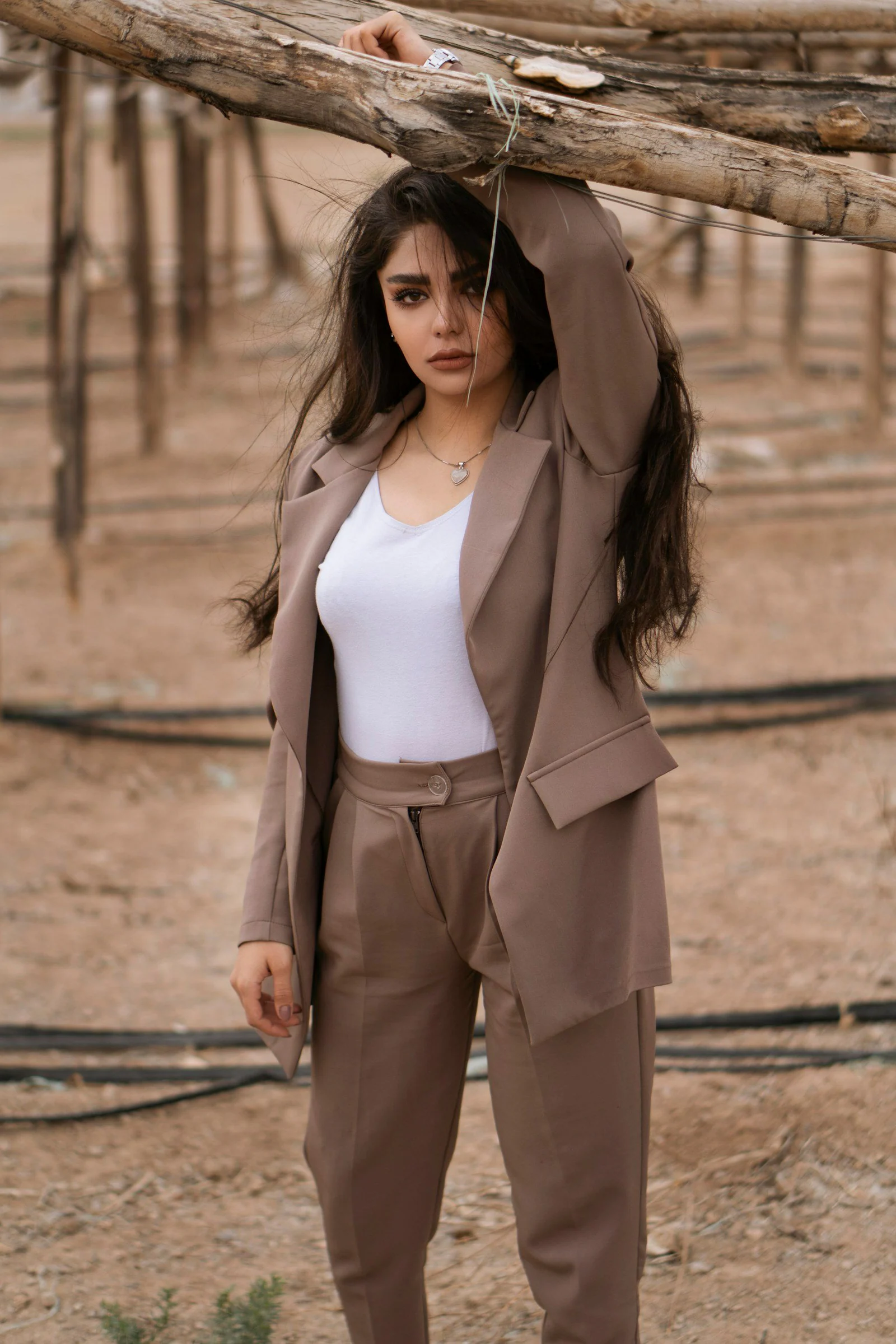 Woman in white tank top and brown coat standing on brown sand during daytime