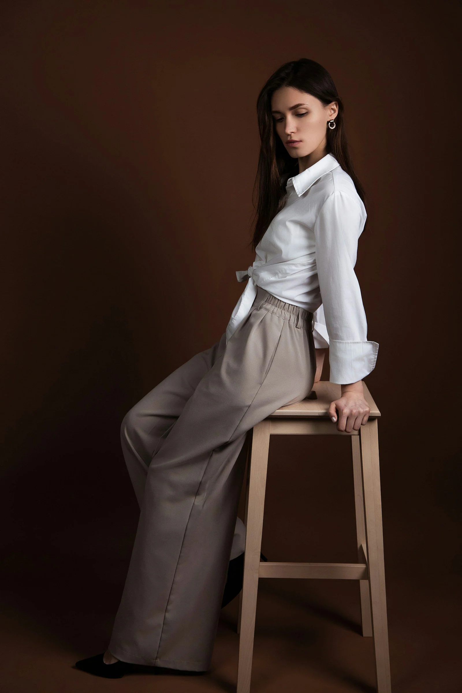 A woman poses elegantly on a wooden stool