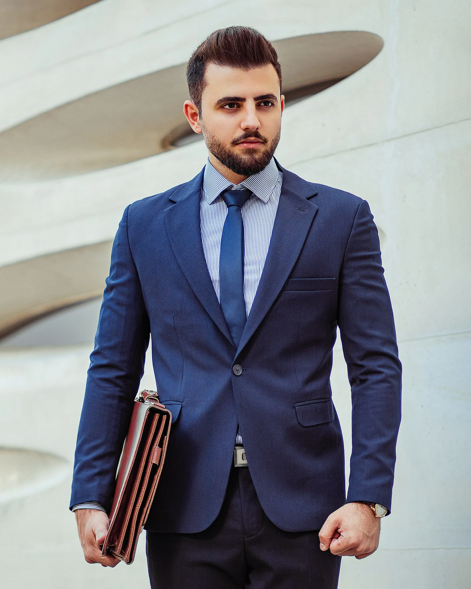 Man in a navy business suit and blue tie carrying a leather folio