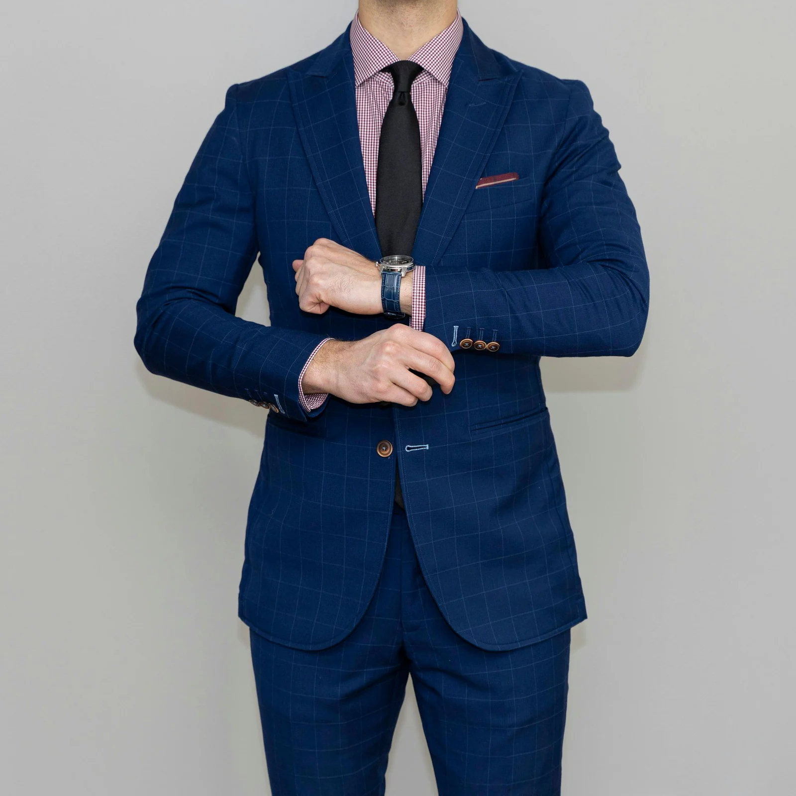 Navy windowpane business suit with a dark tie, adjusting a watch