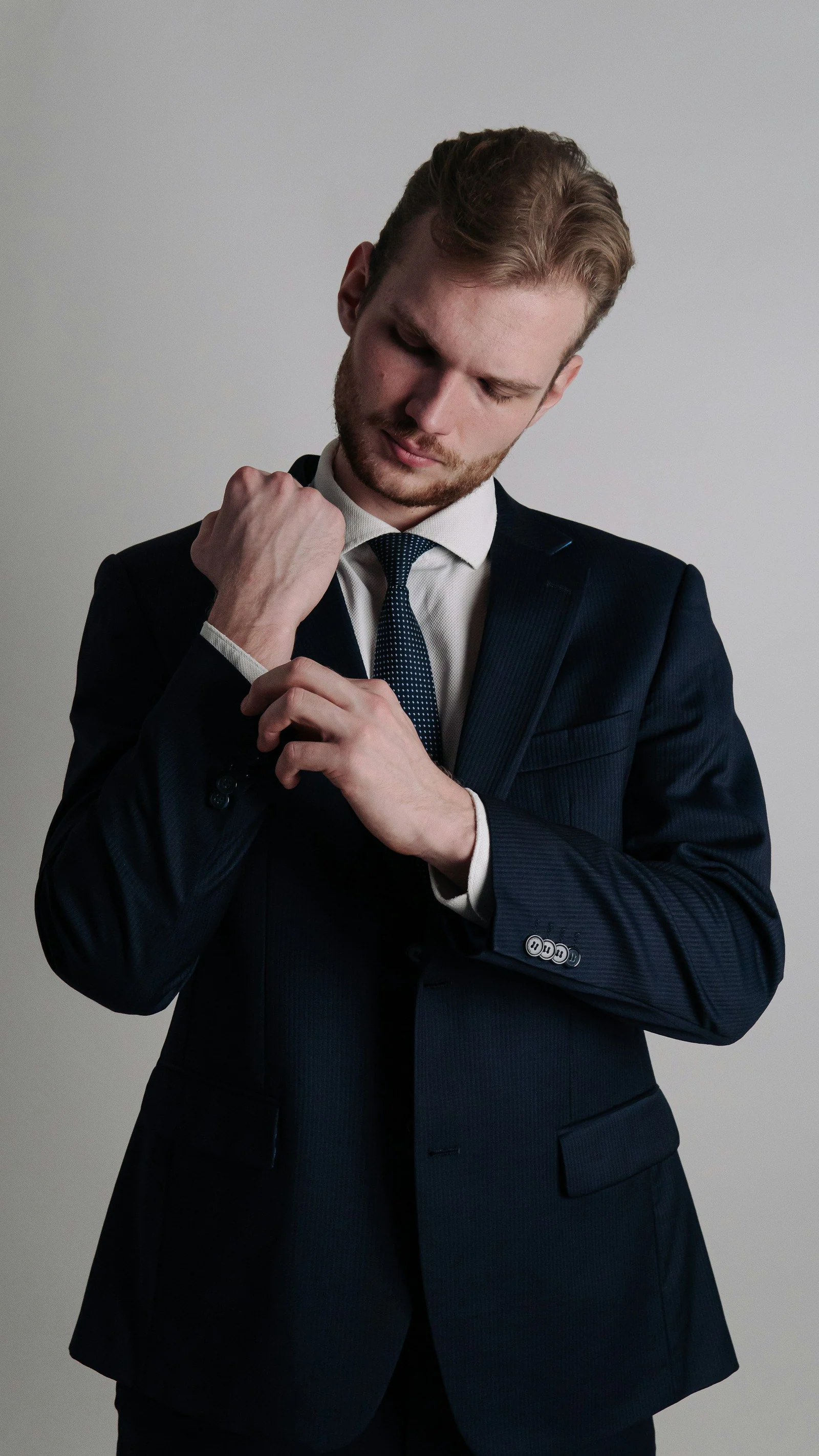 Man adjusting his tie in a dark navy business suit