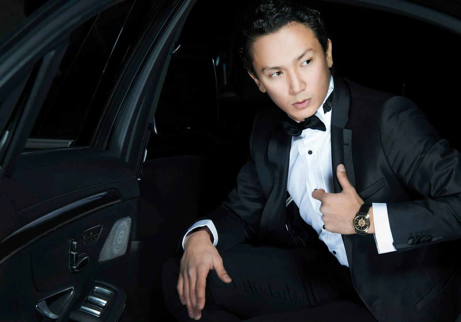 Man in a black dinner suit and bow tie seated in a car