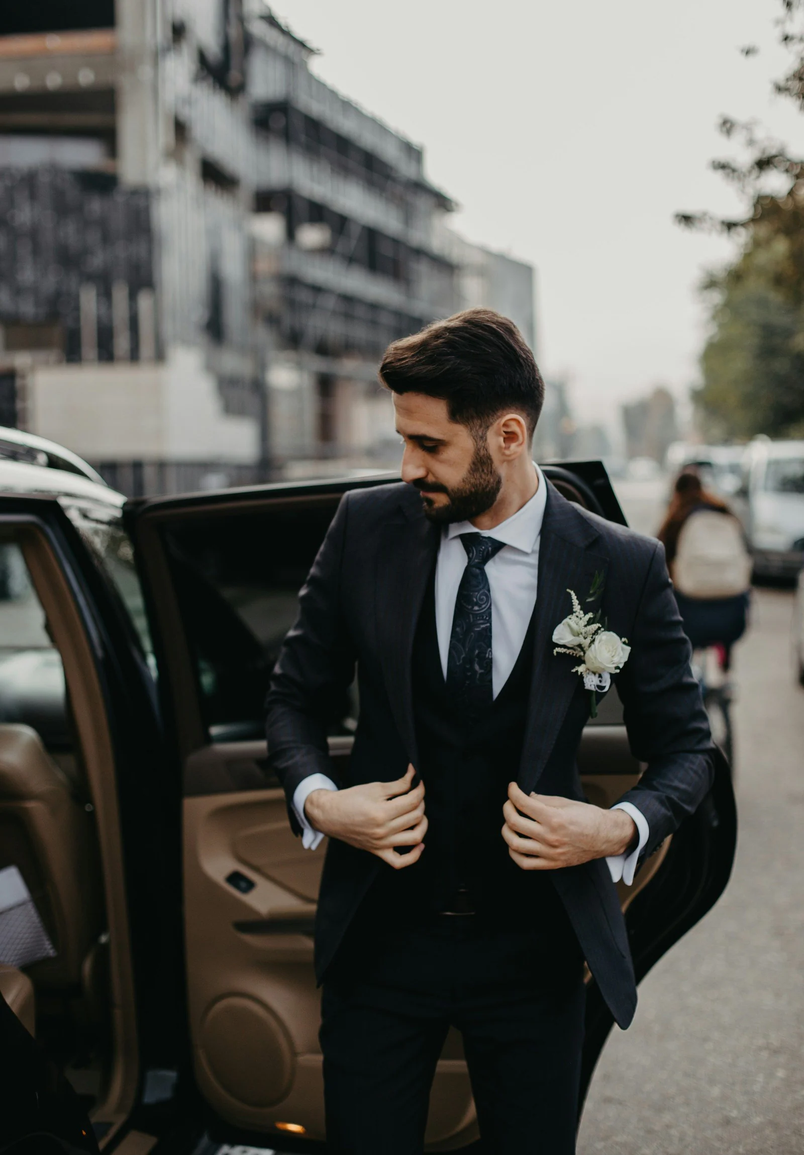 Groom in a black suit beside a car